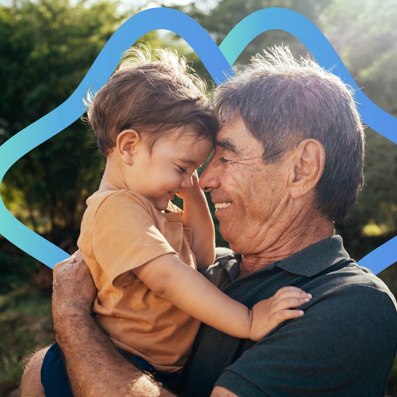 A grandfather embraces his grandson. They are both smiling.